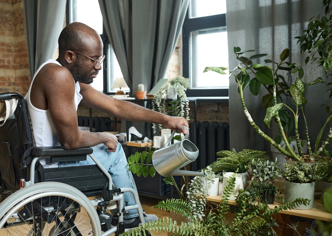 A Man in a wheelchair at home watering his plants